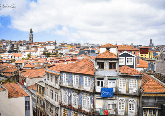 Panoramic view of Porto, Portugal, showcasing traditional tiled buildings with red rooftops and the Clérigos Tower under a partly cloudy sky