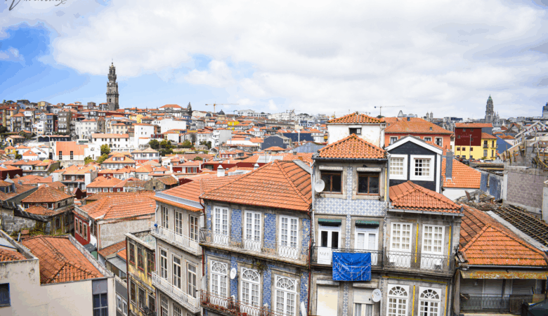 Panoramic view of Porto, Portugal, showcasing traditional tiled buildings with red rooftops and the Clérigos Tower under a partly cloudy sky