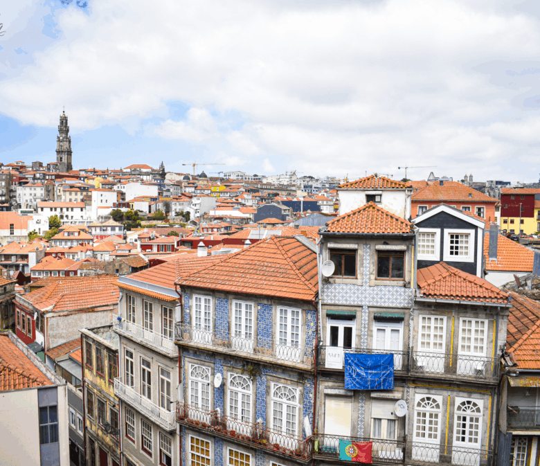 Panoramic view of Porto, Portugal, showcasing traditional tiled buildings with red rooftops and the Clérigos Tower under a partly cloudy sky